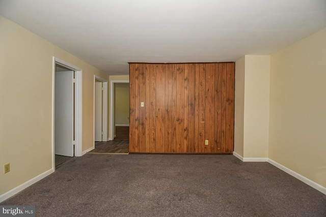 unfurnished room featuring dark colored carpet and wooden walls