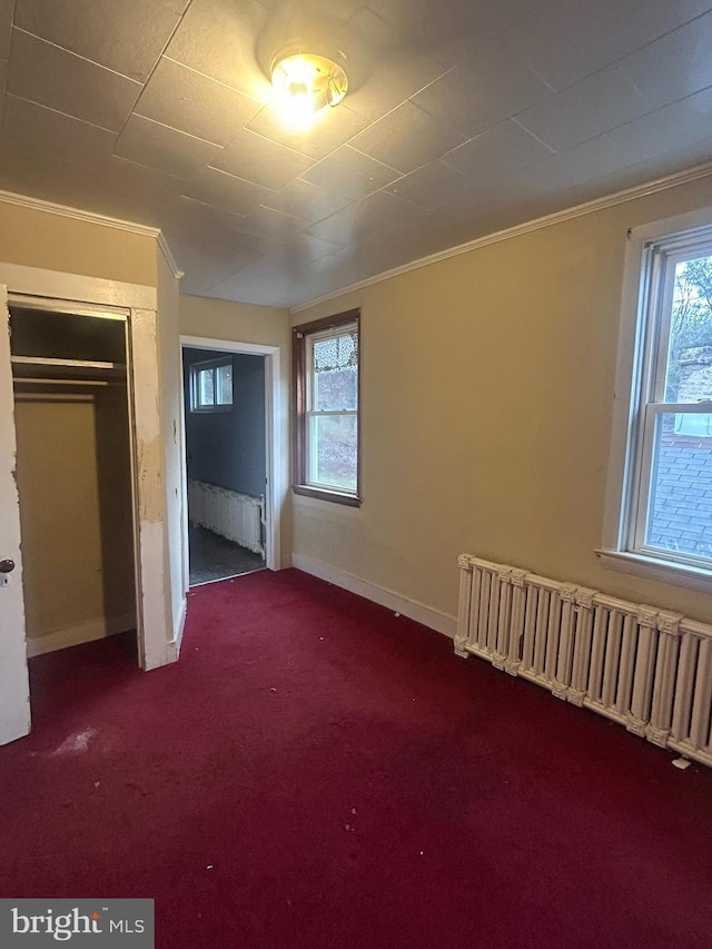 unfurnished bedroom with radiator, a closet, ornamental molding, and dark colored carpet