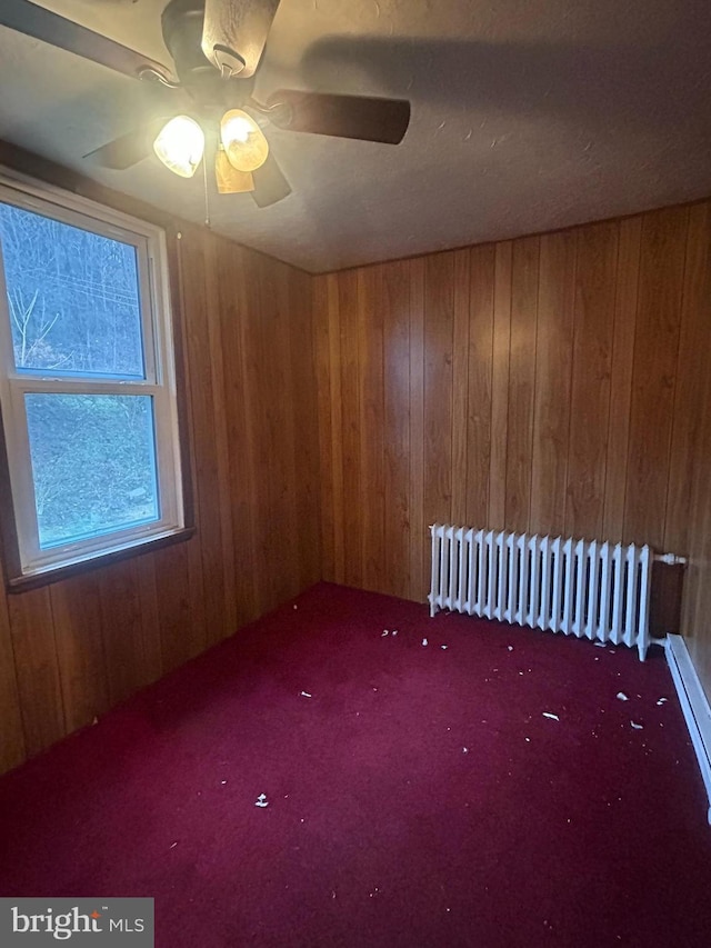 spare room with carpet floors, radiator, wooden walls, and ceiling fan