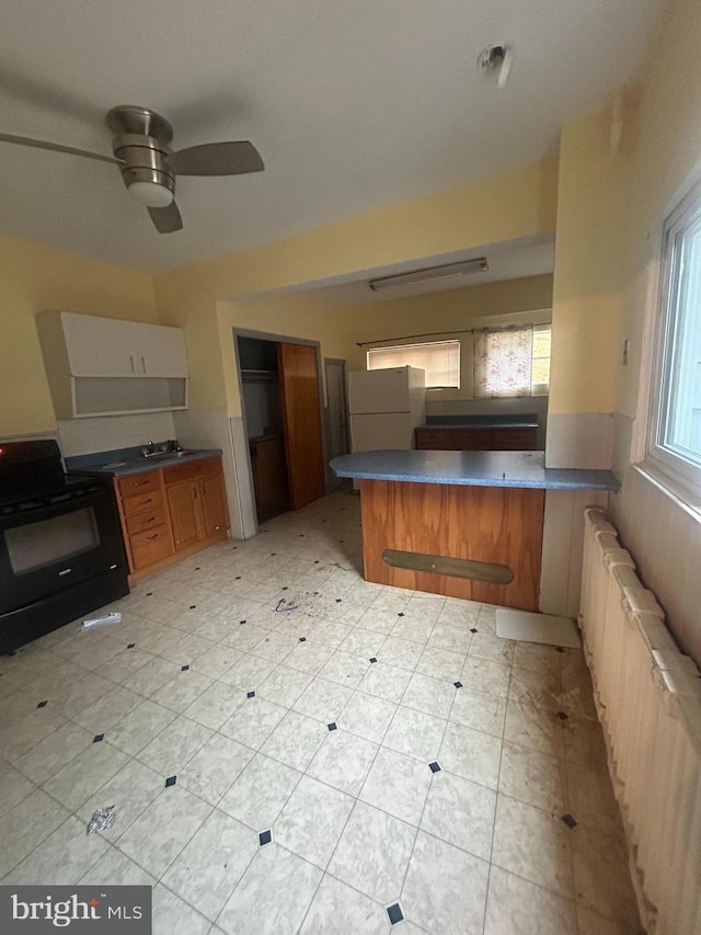 kitchen featuring kitchen peninsula, ceiling fan, electric range, radiator heating unit, and white fridge