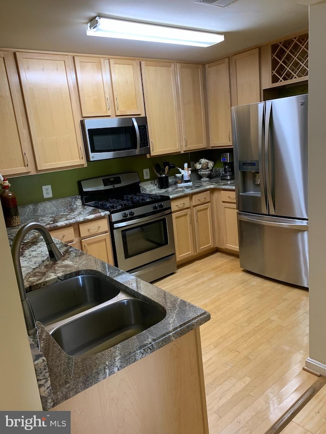 kitchen with sink, light brown cabinets, stainless steel appliances, dark stone counters, and light hardwood / wood-style floors