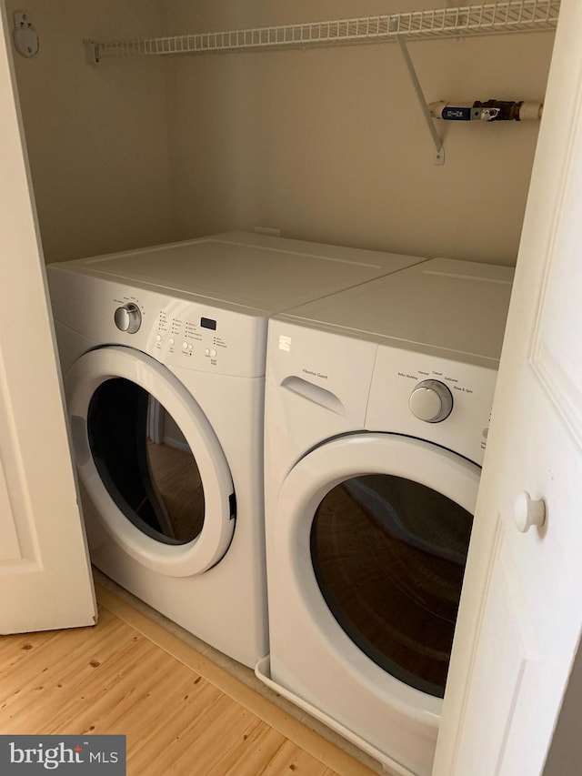 laundry room with washing machine and dryer and light wood-type flooring