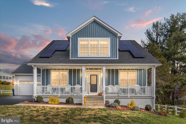 view of front of property with a yard, covered porch, a garage, and solar panels