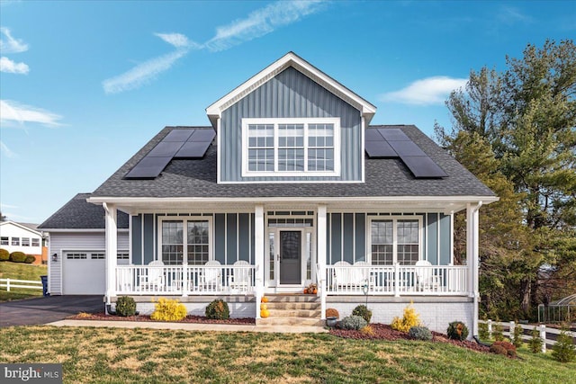 view of front of home with a front lawn, covered porch, a garage, and solar panels