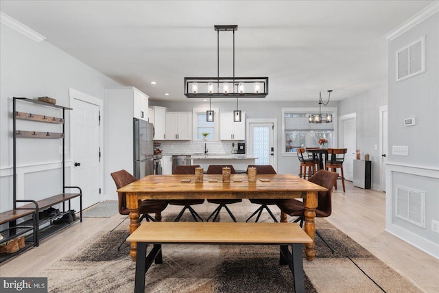 dining space featuring sink, light wood-type flooring, crown molding, and a chandelier