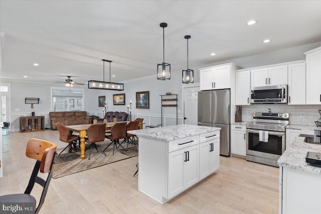 kitchen with light wood-type flooring, stainless steel appliances, ceiling fan, pendant lighting, and a center island