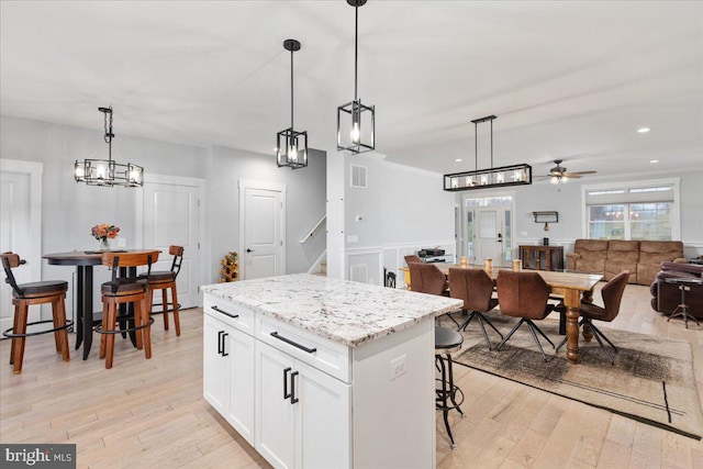 kitchen with light wood-type flooring, ceiling fan, pendant lighting, a center island, and white cabinetry