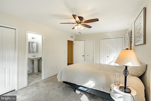 carpeted bedroom with ceiling fan, ensuite bath, multiple closets, and sink