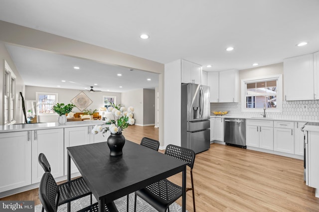 kitchen with decorative backsplash, white cabinets, stainless steel appliances, and light wood-type flooring