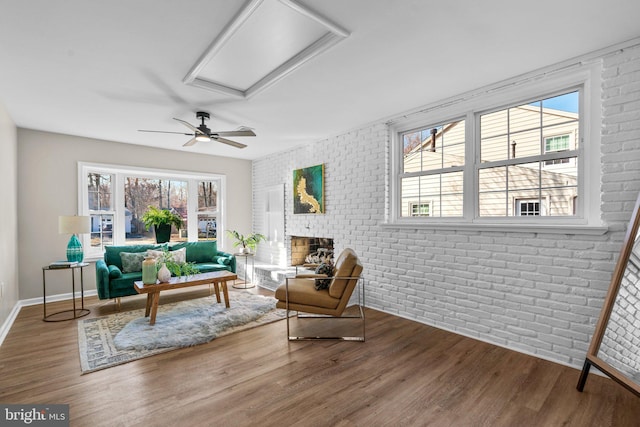 living area with ceiling fan, a fireplace, wood-type flooring, and brick wall