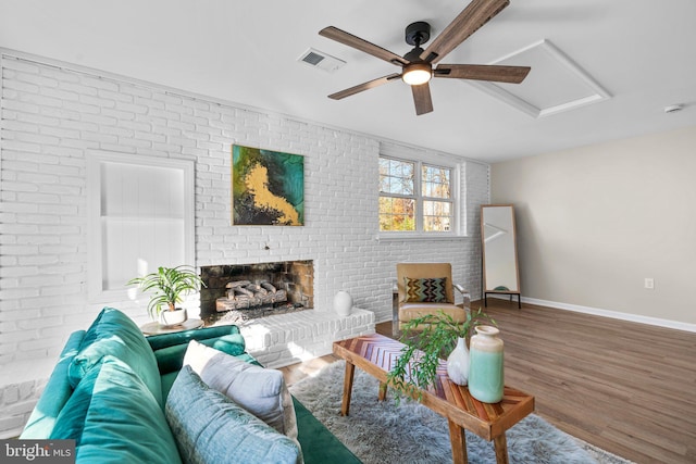 living room with wood-type flooring, a brick fireplace, ceiling fan, and brick wall