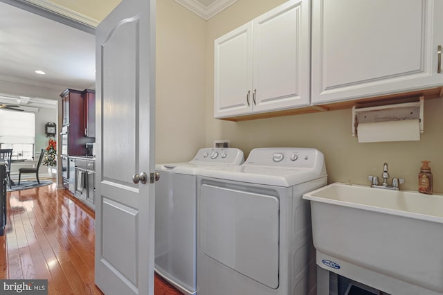 washroom featuring sink, cabinets, separate washer and dryer, wood-type flooring, and ornamental molding