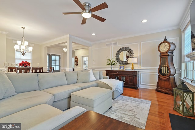 living room featuring ceiling fan with notable chandelier, wood-type flooring, and crown molding