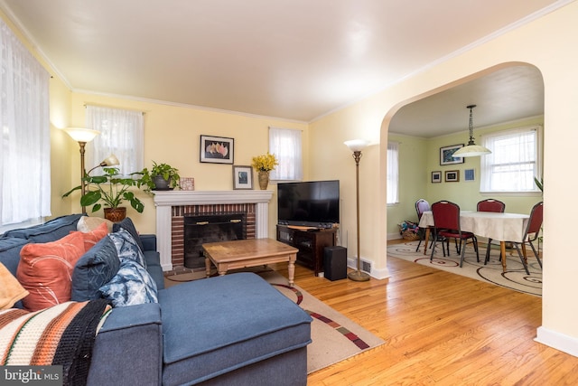 living area featuring baseboards, wood finished floors, arched walkways, and ornamental molding