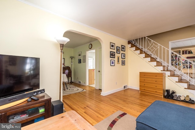 living room with visible vents, wood finished floors, arched walkways, baseboards, and stairs