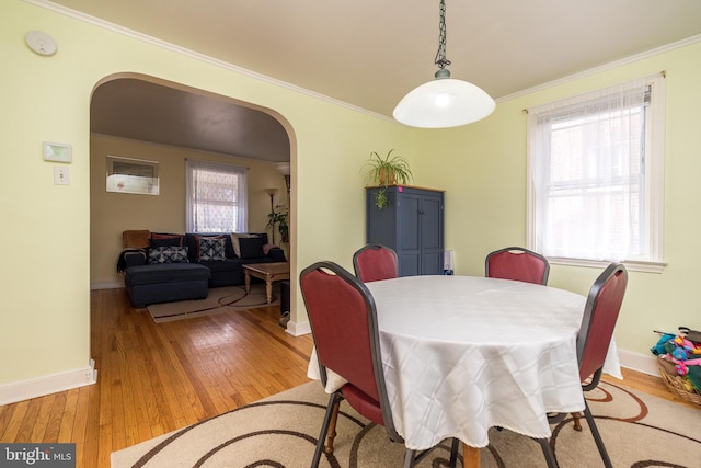 dining room with baseboards, arched walkways, wood-type flooring, and ornamental molding