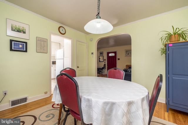 dining area featuring visible vents, arched walkways, light wood-style flooring, and ornamental molding