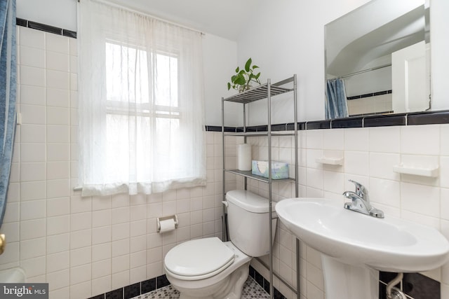 bathroom with a wainscoted wall, toilet, a sink, a shower with shower curtain, and tile walls