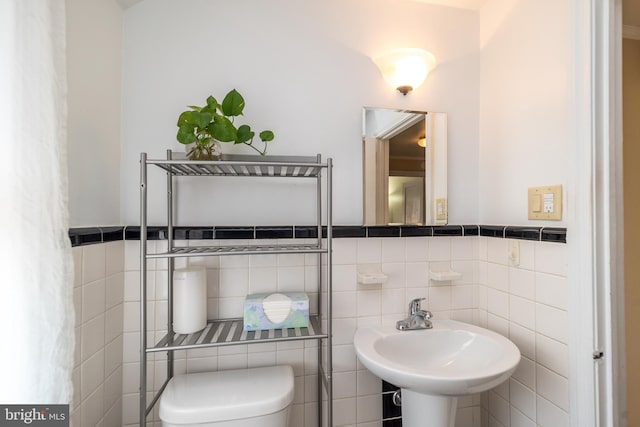 bathroom with wainscoting, toilet, tile walls, and a sink