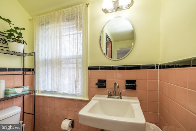 half bathroom featuring a sink, toilet, tile walls, and wainscoting