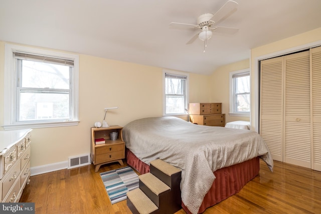 bedroom with wood finished floors, visible vents, baseboards, lofted ceiling, and a closet