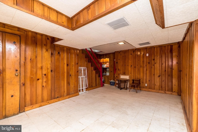 interior space featuring stairway, wooden walls, light floors, and visible vents