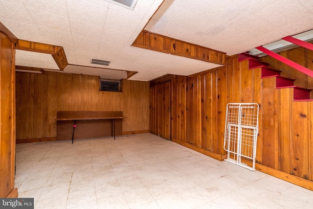 finished basement with tile patterned floors, visible vents, wood walls, and stairway