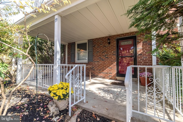 property entrance with brick siding, covered porch, and a carport