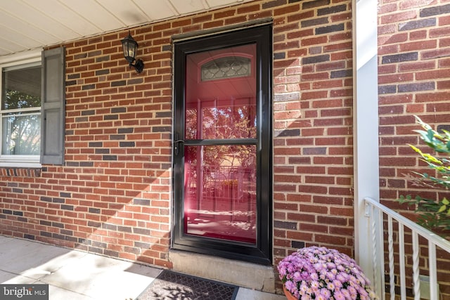 view of exterior entry with brick siding and a porch