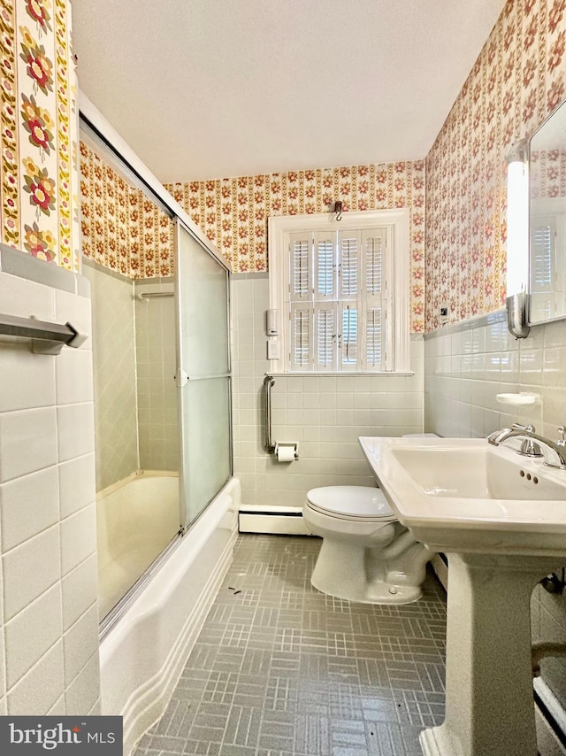 bathroom featuring bath / shower combo with glass door, tile patterned flooring, toilet, tile walls, and baseboard heating