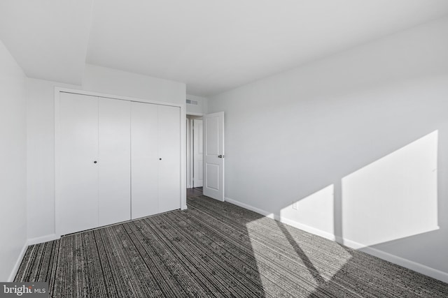 unfurnished bedroom with dark carpet and a closet