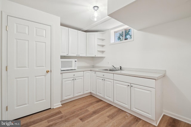 kitchen featuring open shelves, white microwave, white cabinets, and a sink