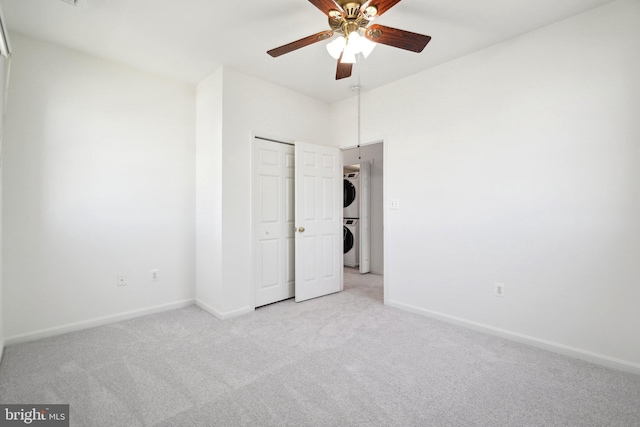 unfurnished bedroom with light carpet, a closet, stacked washer and clothes dryer, and baseboards