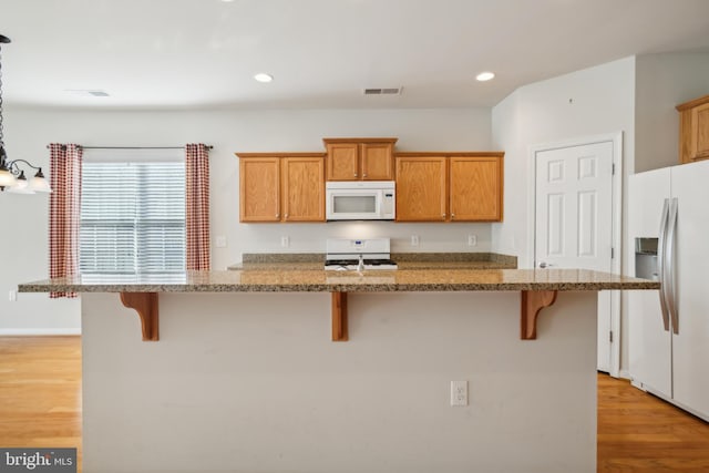 kitchen with light stone counters, white appliances, light hardwood / wood-style floors, a breakfast bar area, and an island with sink