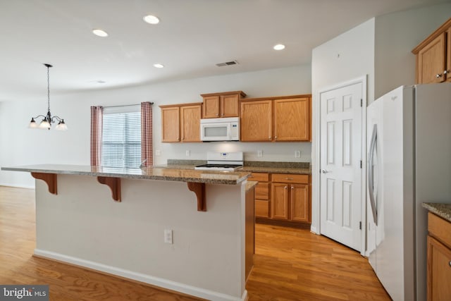 kitchen with a kitchen bar, white appliances, a notable chandelier, light hardwood / wood-style floors, and hanging light fixtures