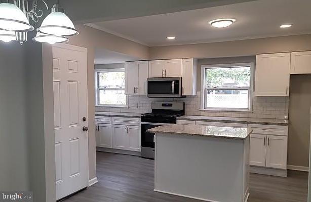 kitchen featuring appliances with stainless steel finishes, decorative light fixtures, white cabinetry, and a wealth of natural light