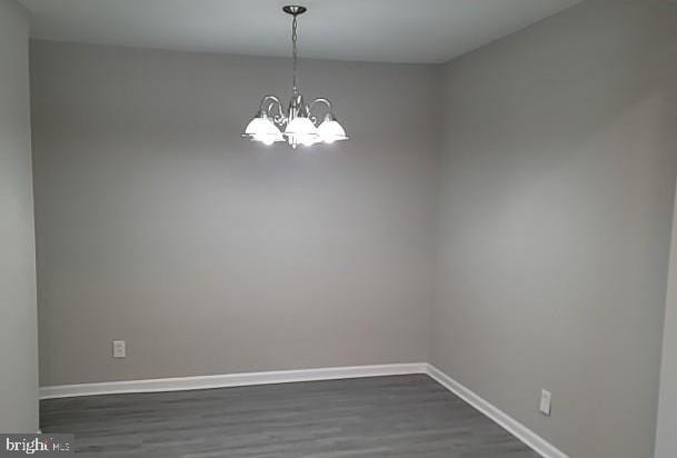 spare room with dark wood-type flooring and a chandelier