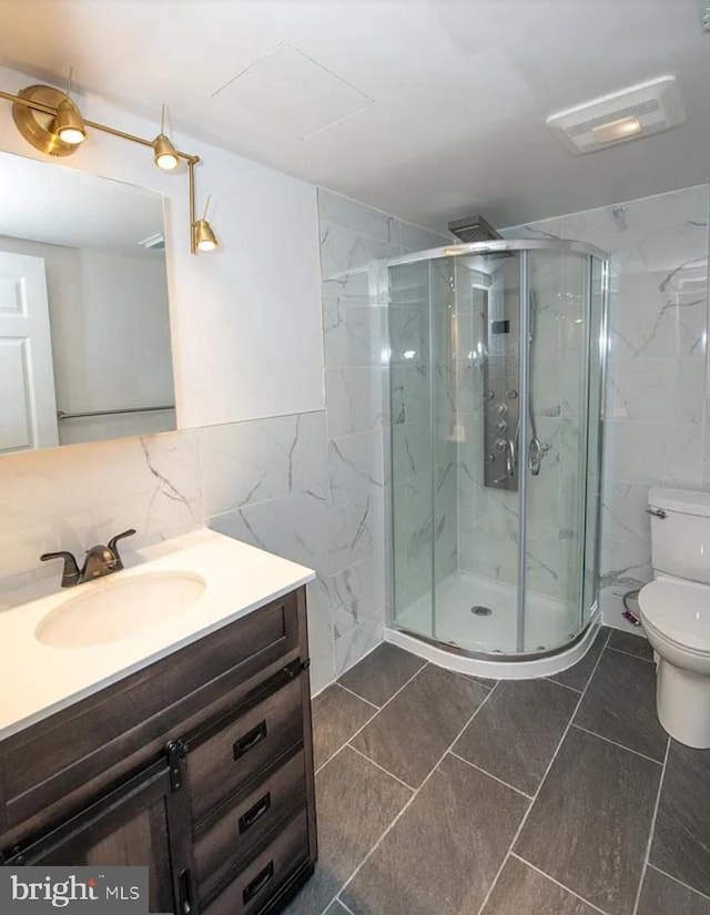 bathroom featuring tile patterned floors, toilet, a shower with door, and tile walls