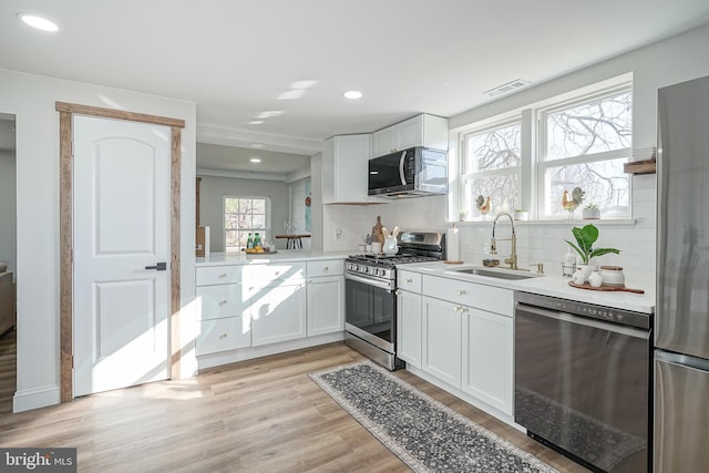 kitchen with sink, decorative backsplash, light wood-type flooring, appliances with stainless steel finishes, and white cabinetry