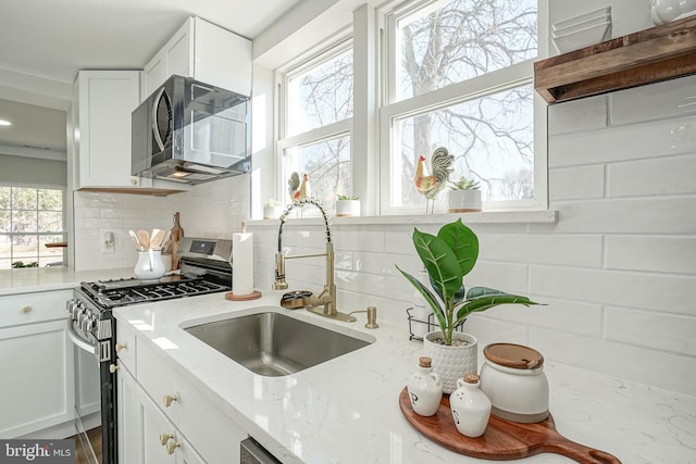 kitchen with stainless steel gas stove, white cabinetry, sink, and a wealth of natural light