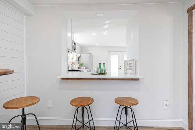 kitchen with white fridge, kitchen peninsula, a breakfast bar area, and white cabinetry