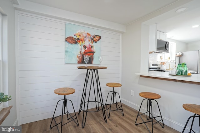 kitchen with a breakfast bar, white cabinetry, white appliances, and light hardwood / wood-style flooring