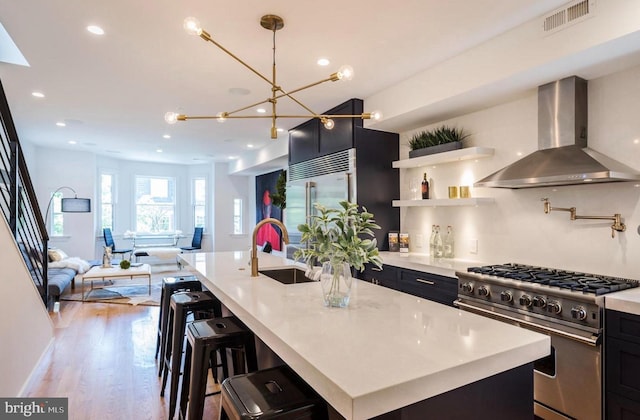 kitchen with sink, a kitchen island with sink, high end appliances, and wall chimney range hood