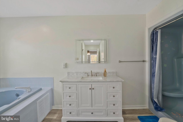 bathroom with wood-type flooring, vanity, and tiled bath