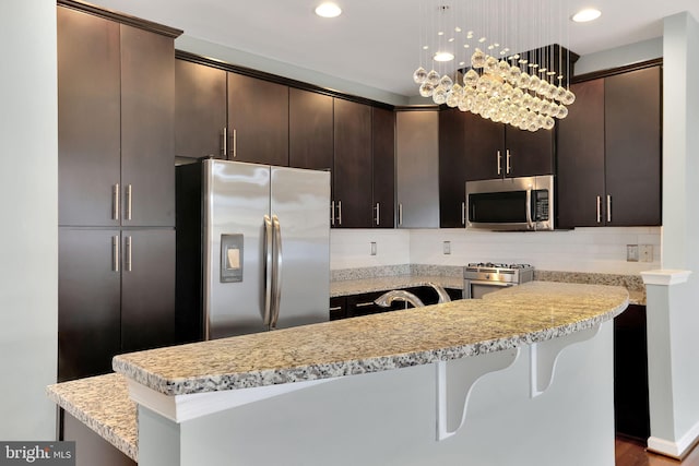 kitchen featuring dark brown cabinetry, tasteful backsplash, pendant lighting, a breakfast bar area, and appliances with stainless steel finishes