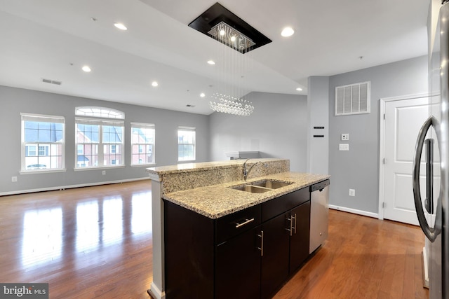 kitchen featuring dark brown cabinetry, sink, stainless steel appliances, wood-type flooring, and a center island with sink