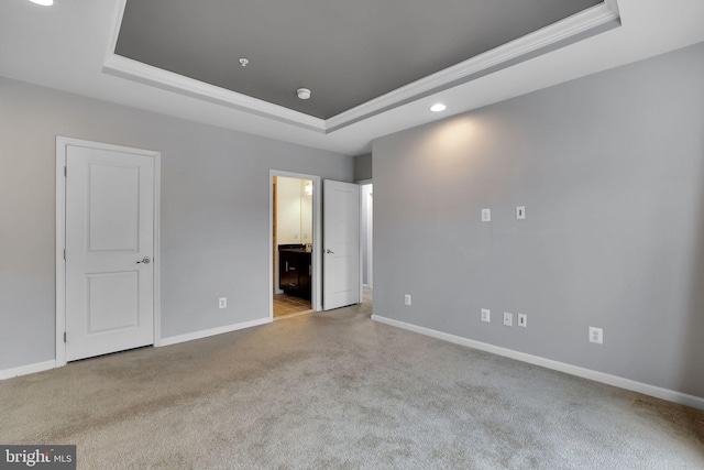 unfurnished bedroom featuring light colored carpet, a tray ceiling, and ensuite bath