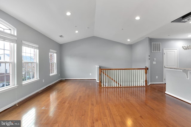 empty room featuring lofted ceiling, a healthy amount of sunlight, and wood-type flooring