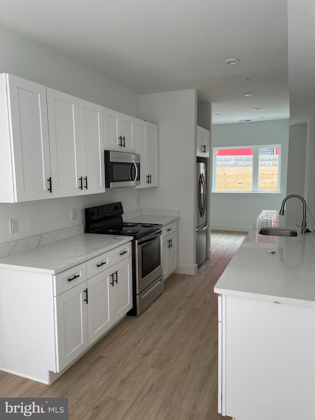 kitchen featuring light stone countertops, white cabinetry, sink, stainless steel appliances, and light hardwood / wood-style flooring