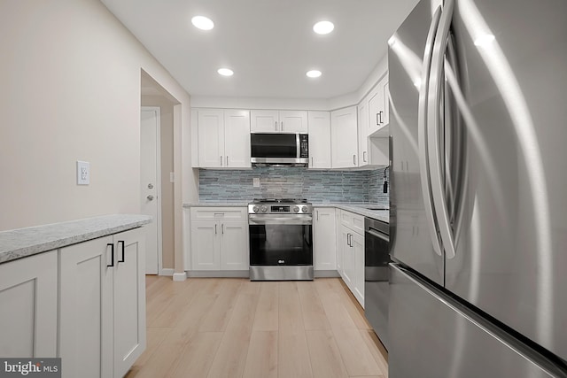 kitchen with light stone countertops, appliances with stainless steel finishes, backsplash, light hardwood / wood-style flooring, and white cabinets